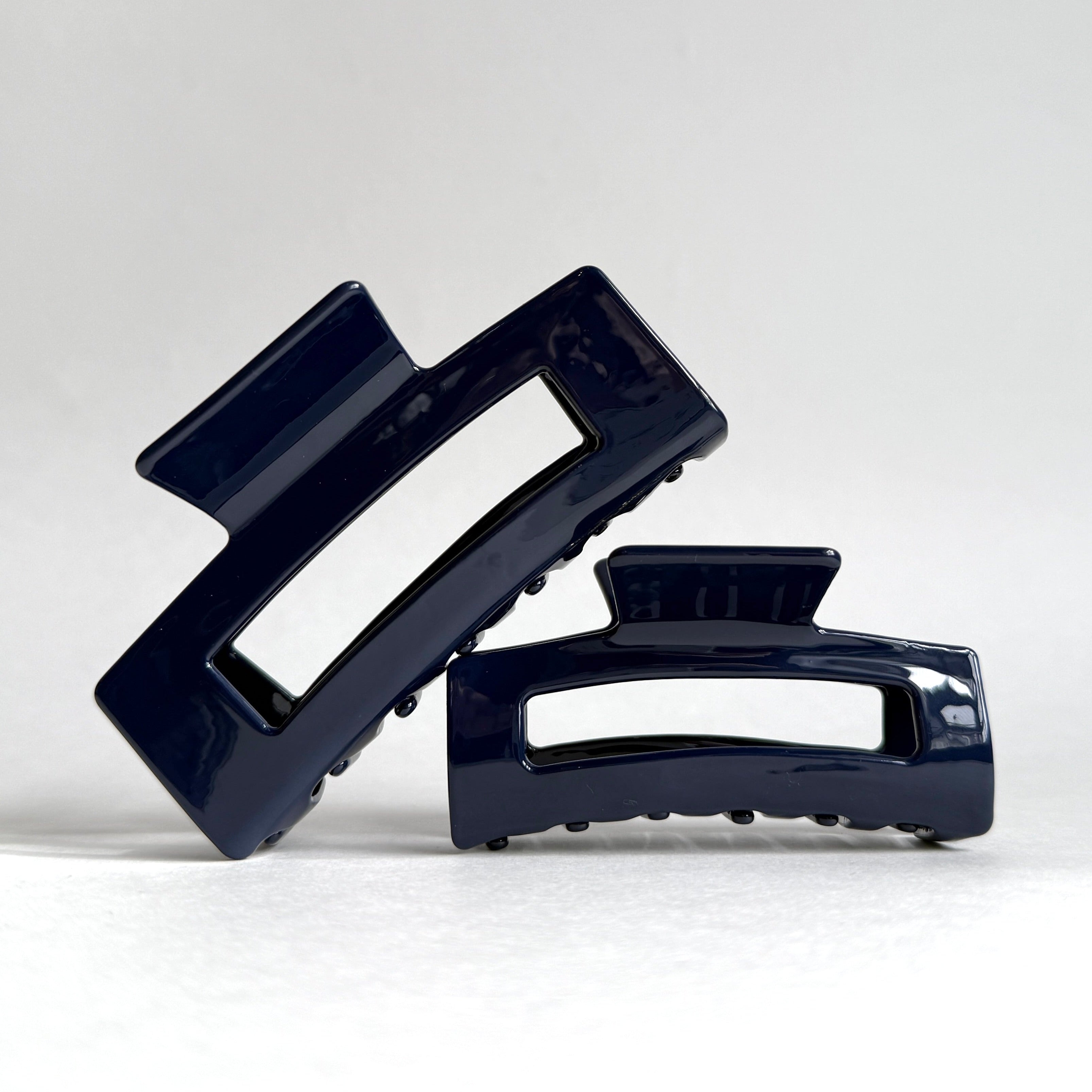 Two navy blue hair clips stacked on a light gray background