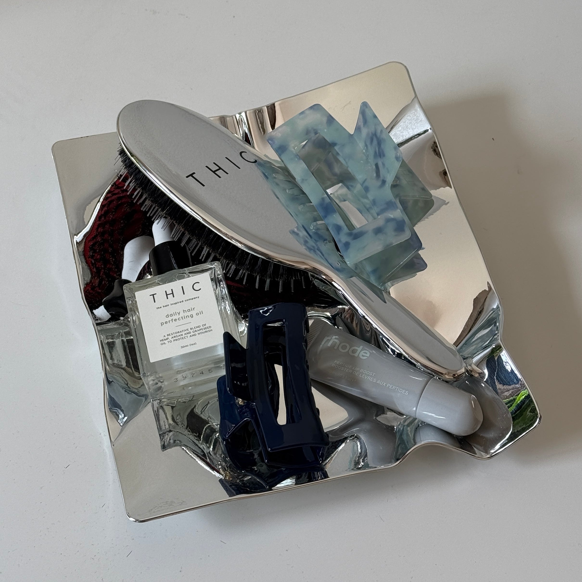 Silver hairbrush and Claw Clips with 'THIC' branding on a reflective surface